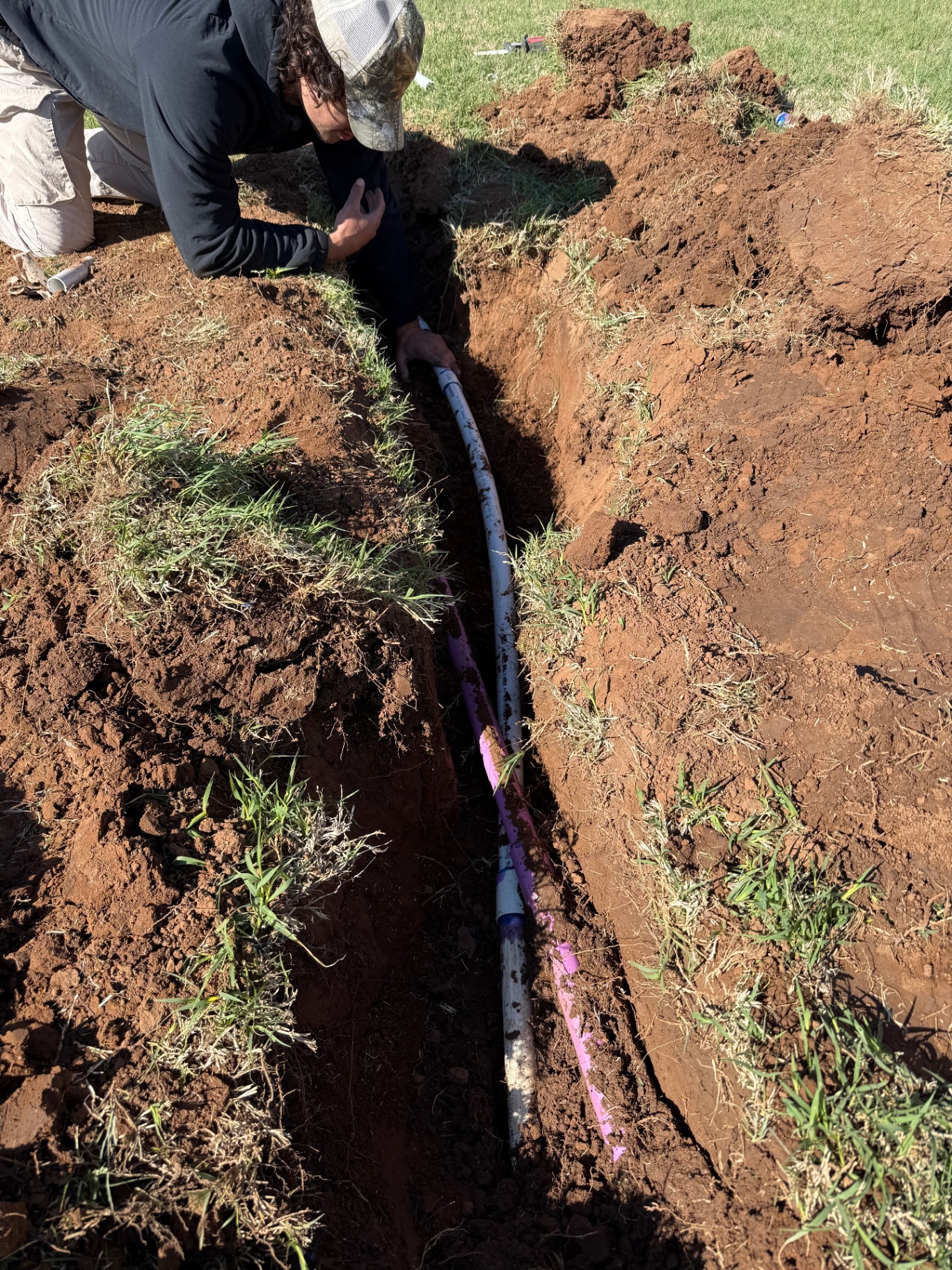 close-up of poly irrigation line running through a fresh red-dirt trench in Tuttle Oklahoma