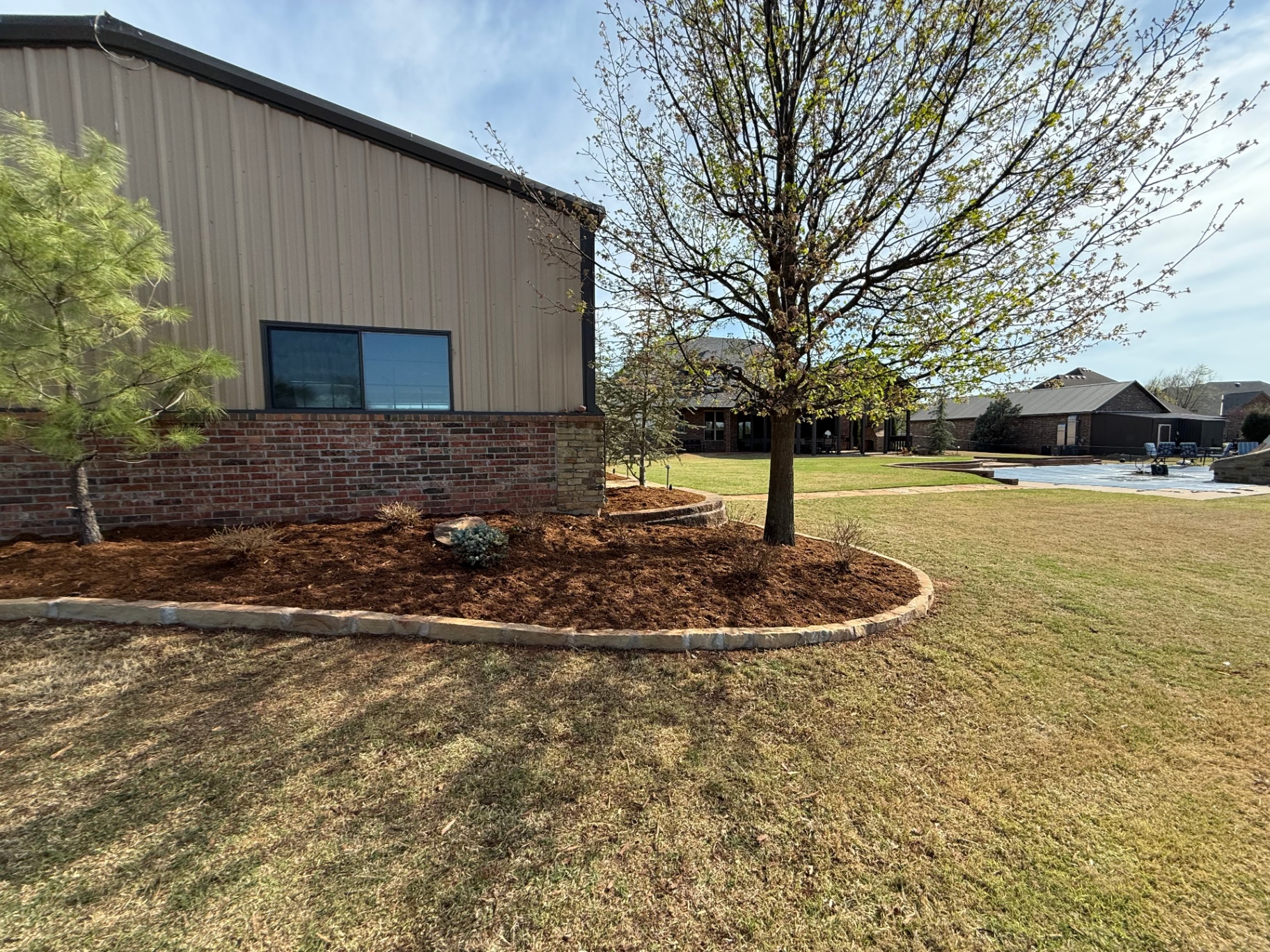 mulch bed wrapping a stacked-stone building corner with shade tree in Tuttle Oklahoma