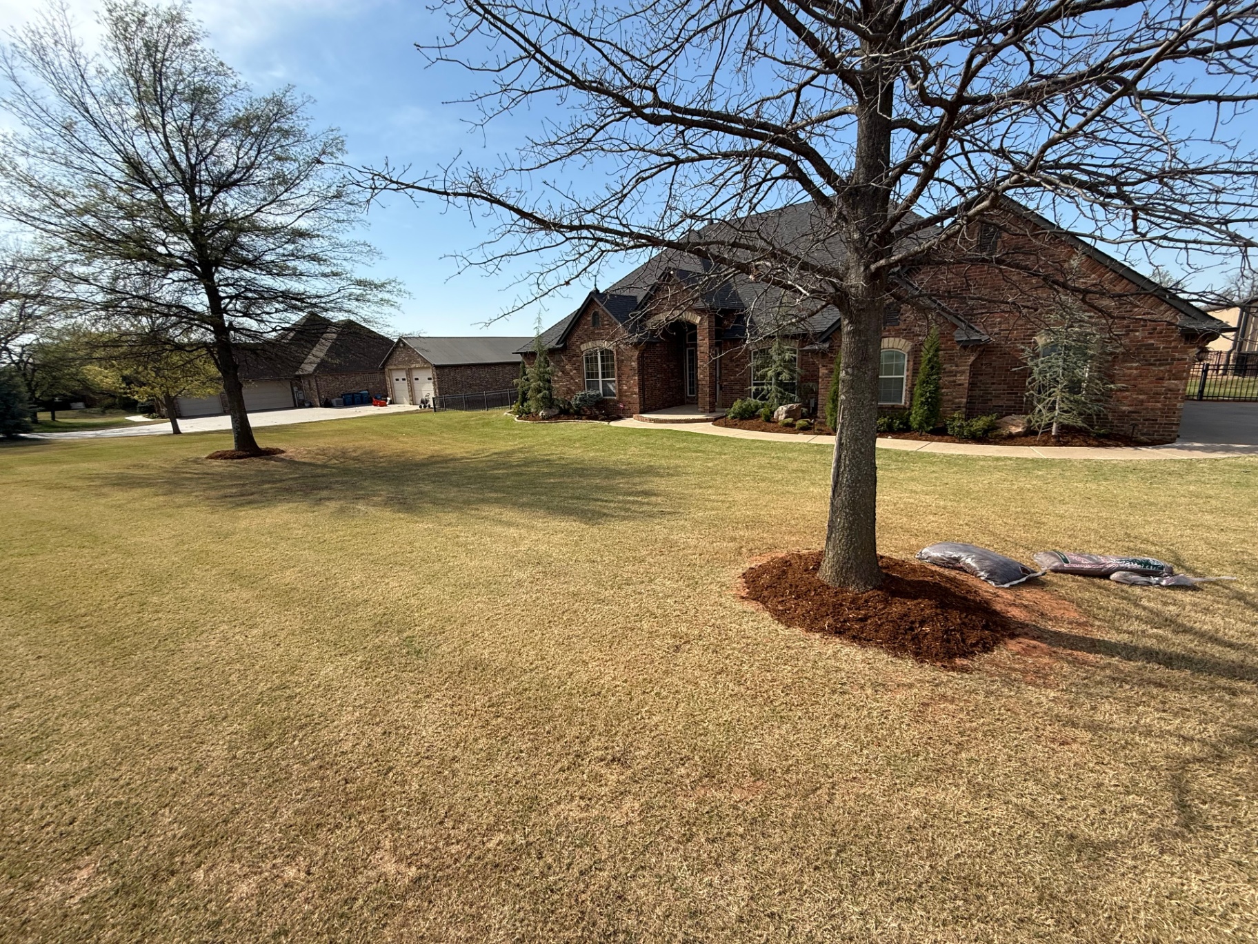 wide view of a brick home front yard after tree mulching and bed cleanup in Tuttle Oklahoma