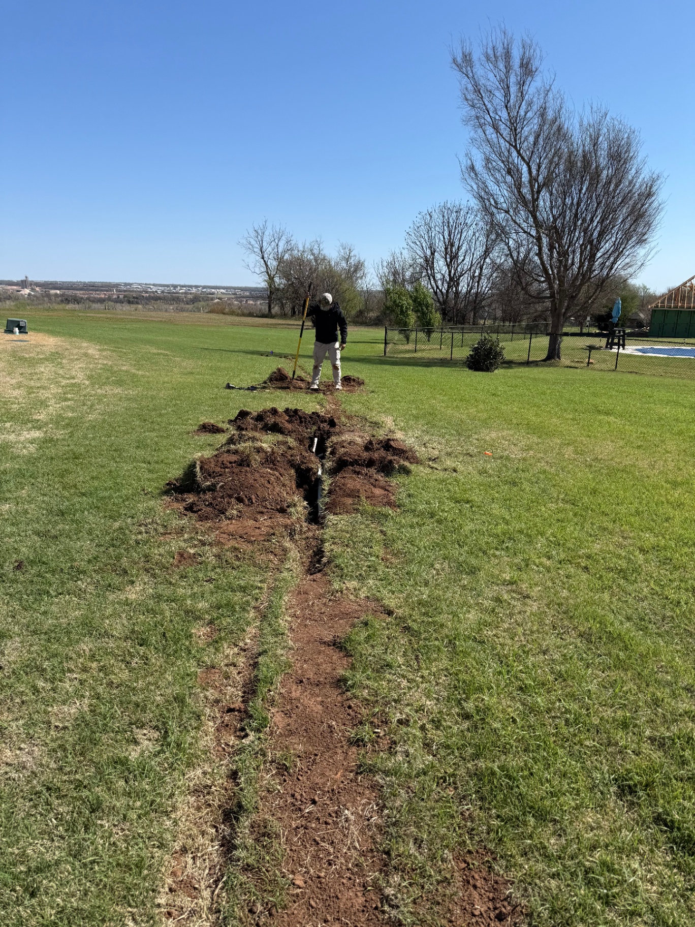 technician standing over a long sprinkler trench running across a large backyard in Tuttle Oklahoma