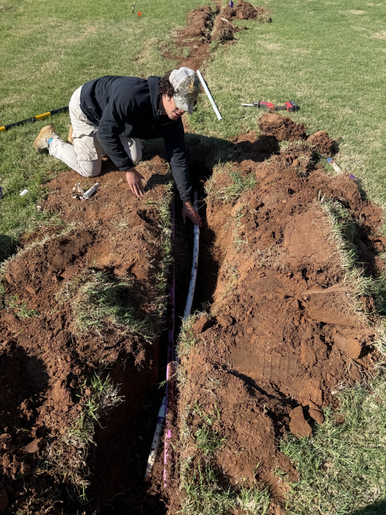 technician setting PVC sprinkler pipe by hand in a narrow lawn trench in Tuttle Oklahoma